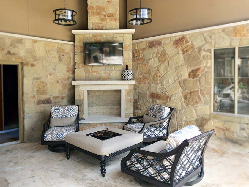 Outdoor natural stone fireplace with wall-mounted tv and sitting area.