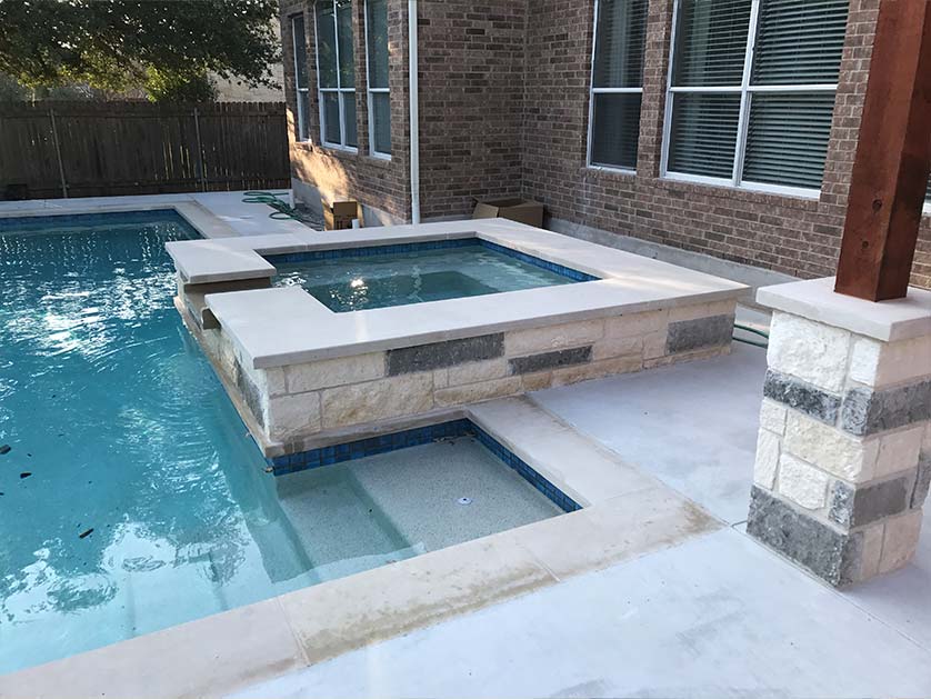 Modern hot tub with overflow waterfall falling into adjacent pool. Custom fire pit feature built next to the hot tub.